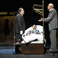 Hercule Poirot diskutiert am Todesbett Ratchetts im Zugabteil mit Monsieur Bouc. Ratchett liegt mit weit geöffneten Augen auf dem Bett.