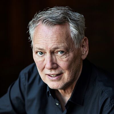 Portraitfoto von Dirk Böhling. Er hat kurzes graues Haar und trägt ein dunkelblaues Hemd. Der Hintergrund ist schwarz.