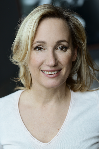 Portraitfoto von Isabel Hindersin. Sie trägt ihr blondes Haar offen, dazu ein weißes Longsleeve. Sie lächelt.