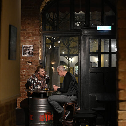 Die beiden Personen sitzen mit einem Getränk am Tisch.