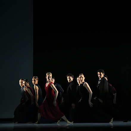 Alle Tänzer:innen sind auf der Bühne. Zwei Tänzerinnen sind rot gekleidet.