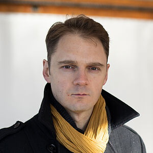 Portraitfoto von Luc Durand in schwarzem Mantel und gelben Schal