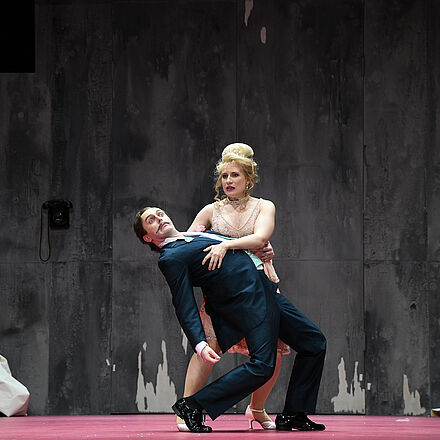 Eine Frau hält einen Mann fest, während im Hintergrund wieder Chaos herrscht.