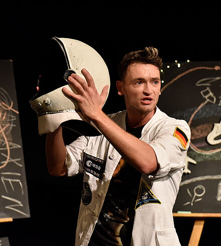 Prof. Blastow hält einen Astronautenhelm empor.
