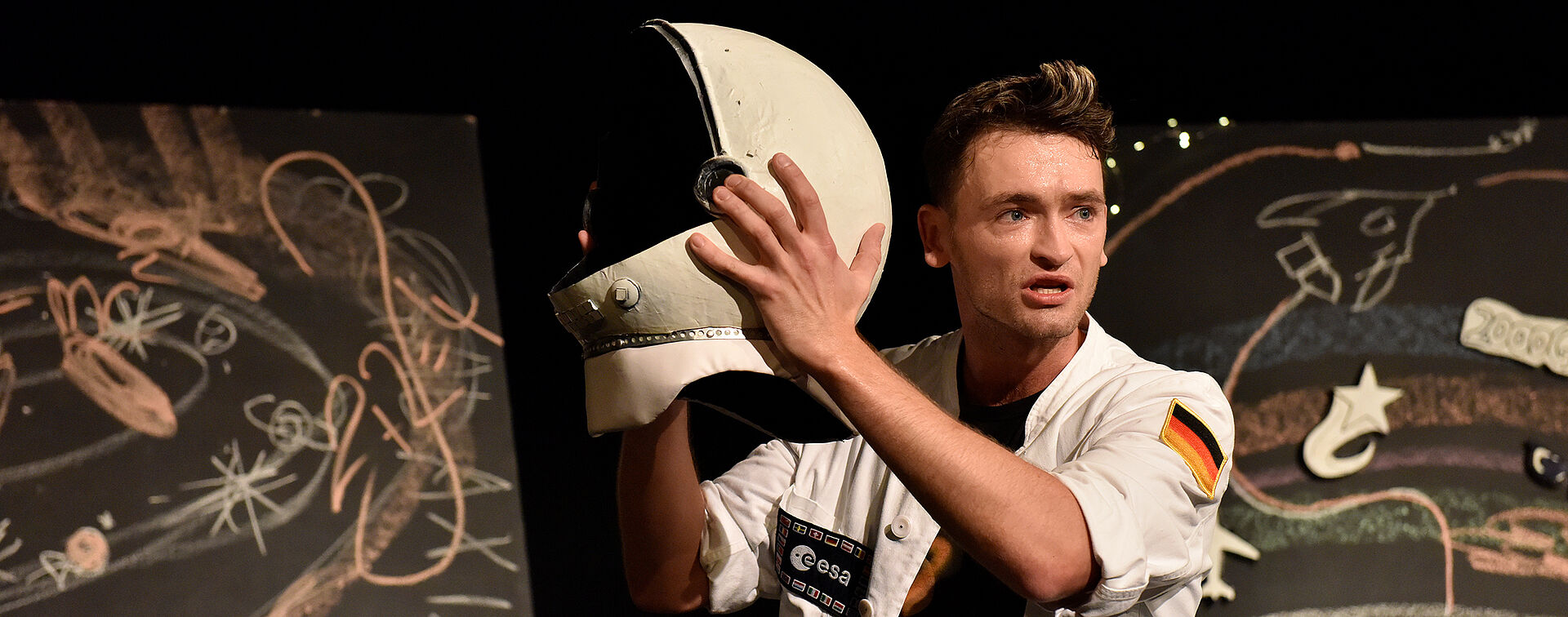 Prof. Blastow hält einen Astronautenhelm empor.