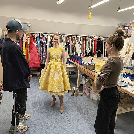 Celen Pieper trägt das gelbe Kleid der Brenda Strong. Der Kostümbildner und eine Schneiderin schauen sich ihr Werk an.