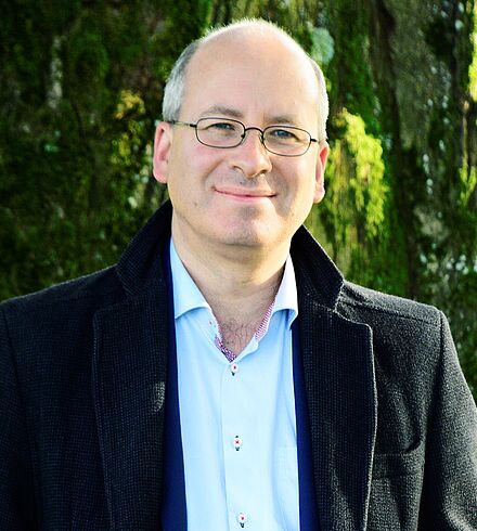 Ein Mann mit wenig Haaren und Brille lächelt in die Kamera