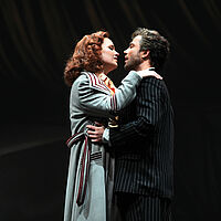 Floria Tosca und Mario Cavaradossi umarmen einander und blicken sind in die Augen. Ihre Hände liegen auf seinen Schultern, er umgreift ihre Hüfte.