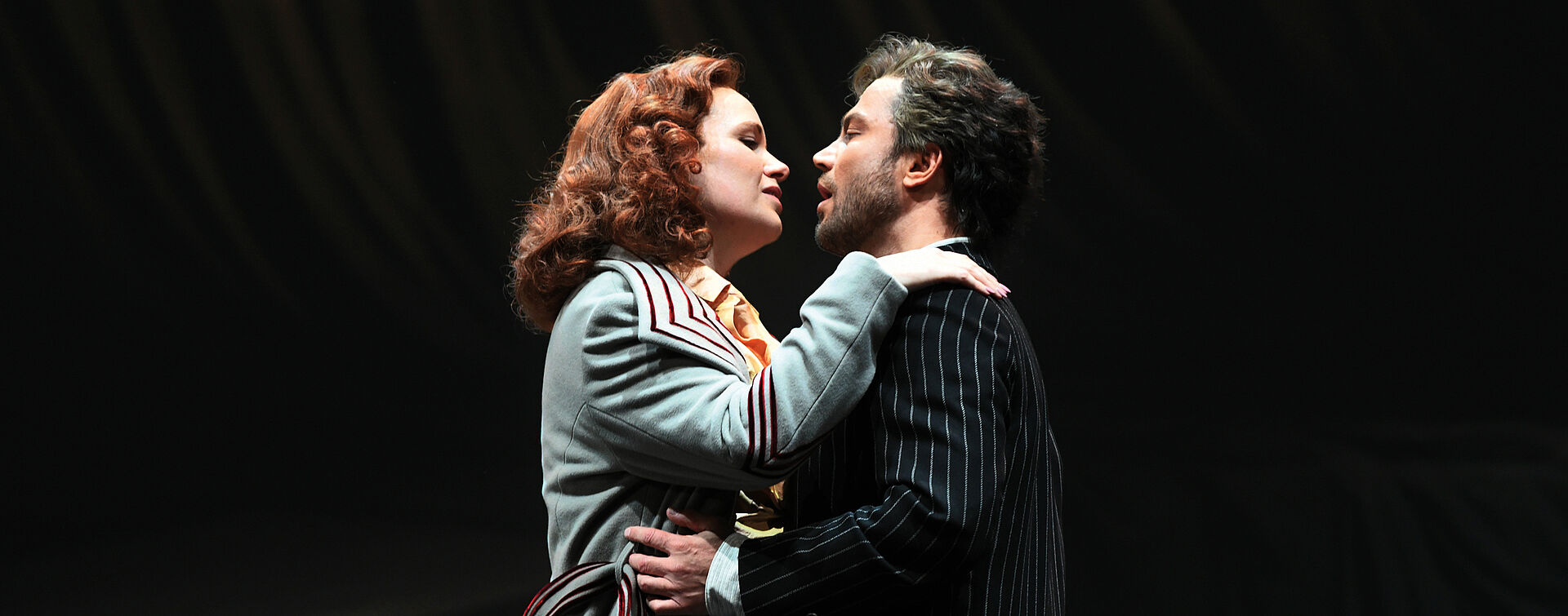 Floria Tosca und Mario Cavaradossi umarmen einander und blicken sind in die Augen. Ihre Hände liegen auf seinen Schultern, er umgreift ihre Hüfte.