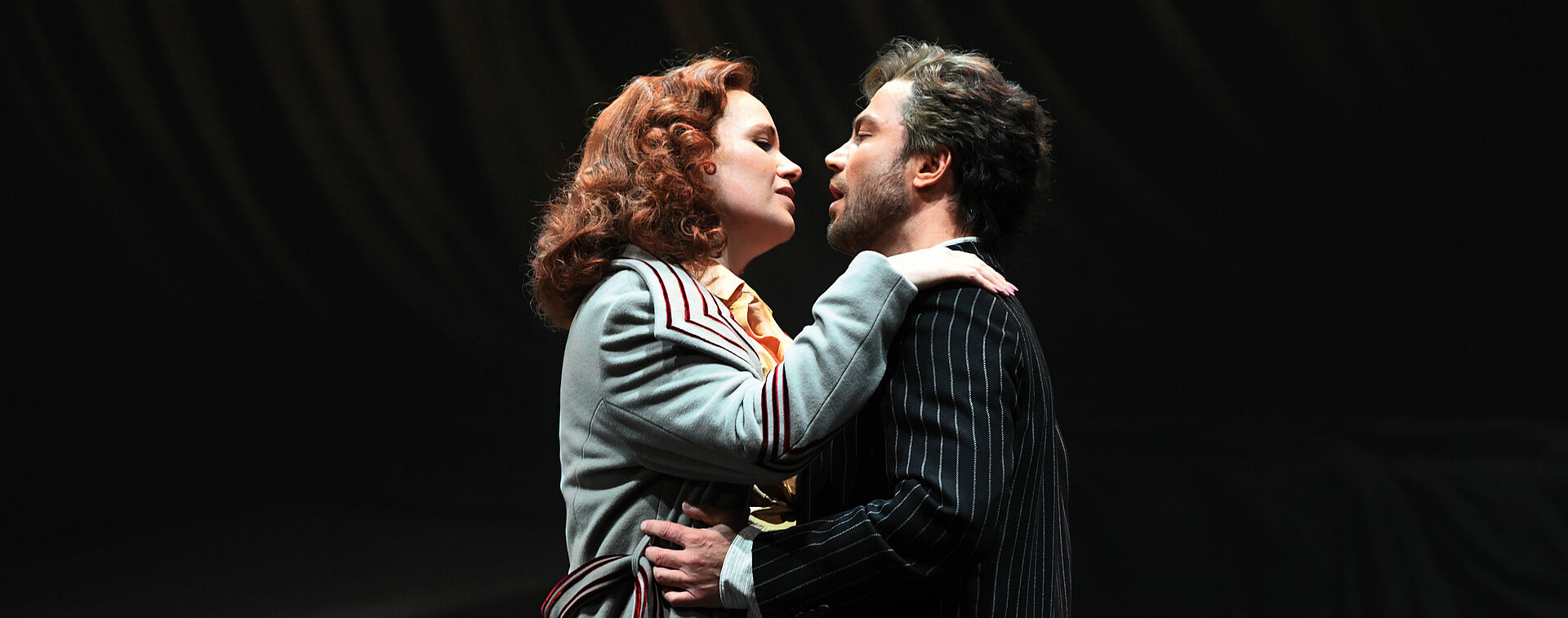 Floria Tosca und Mario Cavaradossi umarmen einander und blicken sind in die Augen. Ihre Hände liegen auf seinen Schultern, er umgreift ihre Hüfte.
