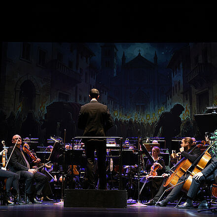 Zwei Personen stehen im Licht, die Atmosphäre ist dunkel und geheimnisvoll.  