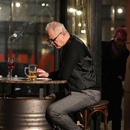 Ein Mann sitzt am Tisch. Die Frau kommt durch die Tür herein.