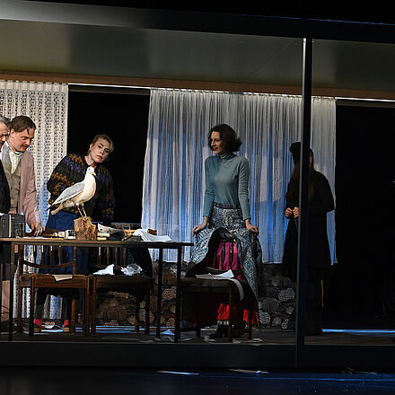 Auf dem Tisch steht eine Möwe. Die Personen schauen sie fragend an.