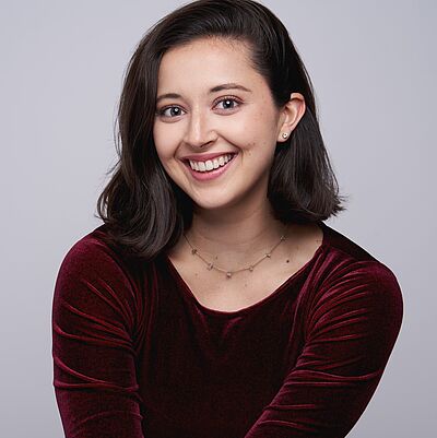 Portraitfoto von Nadja Kilchherr.  Sie hat schulterlange braune Haare. Sie trägt ein weinrotes Samt-T-Shirt und lächelt.