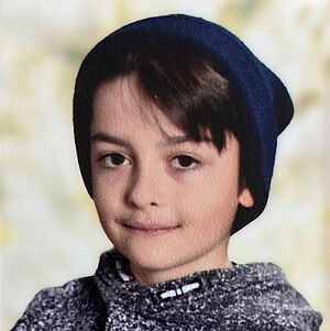 Portraitfoto von Paul Dimitrov. Er trägt eine blaue Mütze, darunter schaut sein dunkelbraunes Haar hervor. Er ist in einen grau-weiß gesprenkelten Hoodie gekleidet.