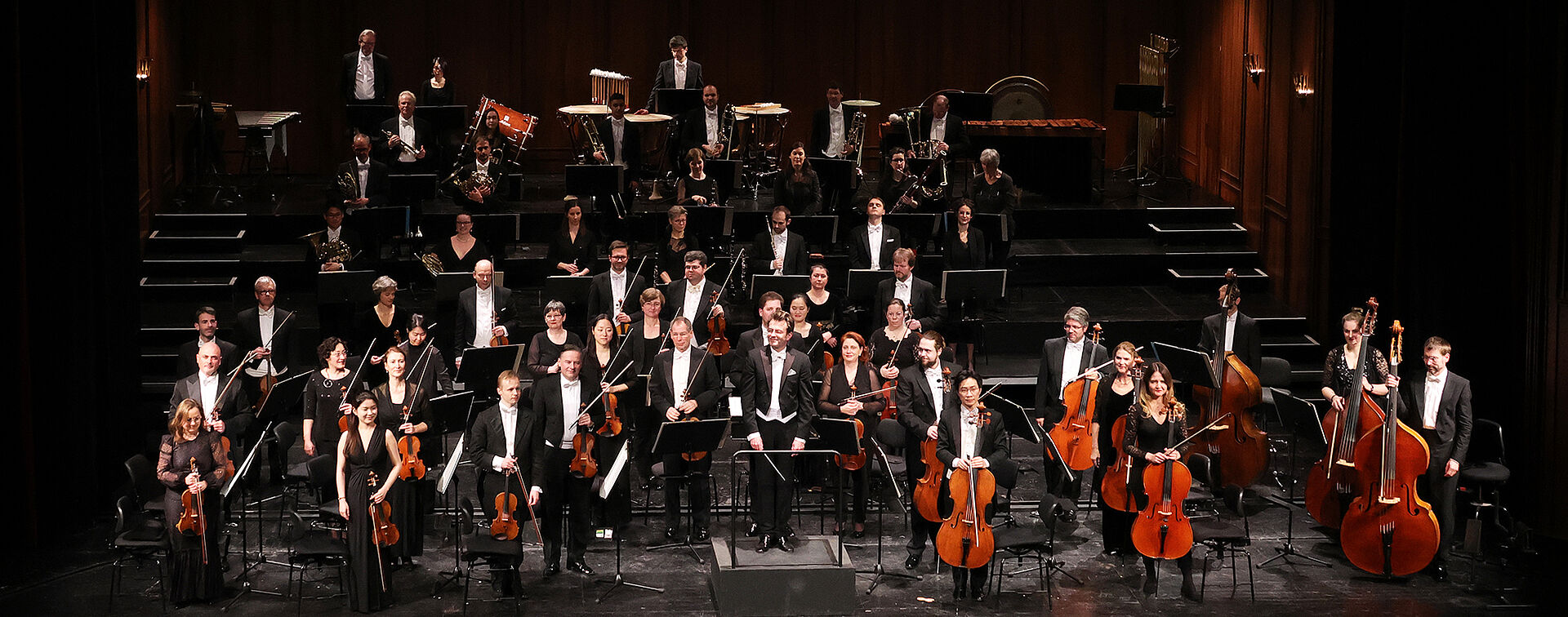 Das Philharmonische Orchester Bremerhaven auf der Bühne des Großen Hauses des Stadttheaters Bremerhaven. Sie stehen mit ihren Instrumenten Richtung Besuchersaal gewandt und lächeln. Sie tragen Konzertkleidung.