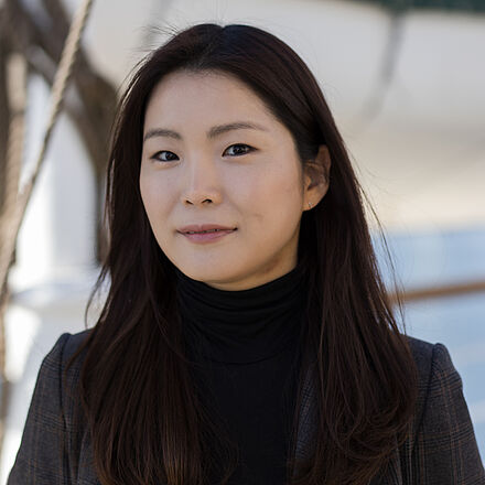 Portraitfoto von Hyejung Park. Sie trägt einen schwarzen Rollkragenpullover, darüber ein schwarzer Blazer. Ihr schwarzes Haar ist glatt und brustlang.