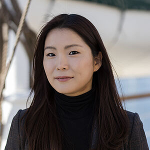 Portraitfoto von Hyejung Park. Sie trägt einen schwarzen Rollkragenpullover, darüber ein schwarzer Blazer. Ihr schwarzes Haar ist glatt und brustlang.