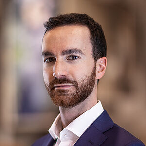 Portraitfoto von Davide Perniceni. Er trägt ein weißes Hemd mit leicht aufgestelltem Kragen, darüber ein dunkelviolettes Jackett.