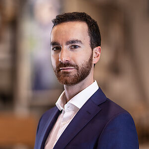 Portraitfoto von Davide Perniceni. Er trägt ein weißes Hemd mit leicht aufgestelltem Kragen, darüber ein dunkelviolettes Jackett.