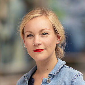 Protraitfoto von Justine Wiechmann. Sie hat blondes Haar, das sie im Nacken zum Dutt gebunden hat. Sie ist in eine Jeansjacke gekleidet.