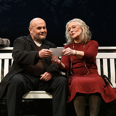 Ein Mann und eine Frau sitzen auf der Bank, sie schauen gemeinsam auf ein Foto