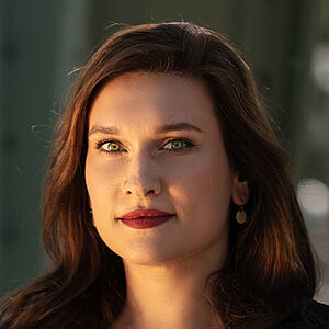 Portraitfoto von Boshana Milkov. Sie trägt einen roten Lippenstift und ihr braunes langes Haar offen. Dazu eine schwarte Bluse, darüber einen schwarzen Blazer. 