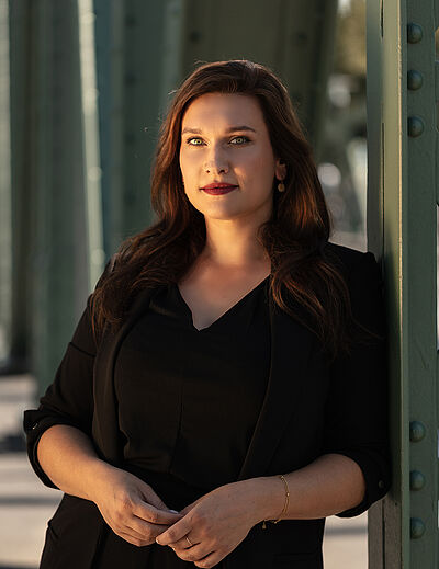 Portraitfoto von Boshana Milkov. Sie trägt einen roten Lippenstift und ihr braunes langes Haar offen. Dazu eine schwarte Bluse, darüber einen schwarzen Blazer.