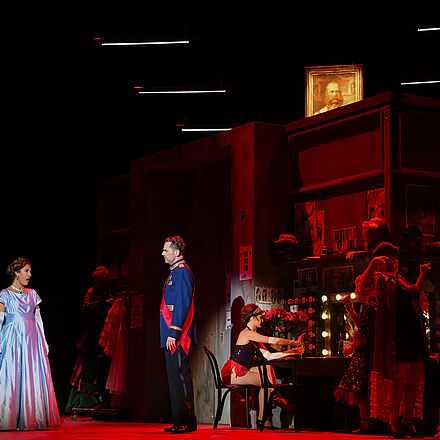 Zwei Personen stehen im Rampenlicht auf einer roten Bühne.