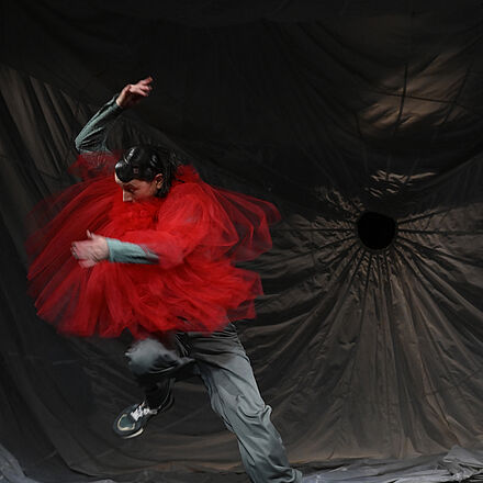 Eine Frau trägt ein rotes Kostüm. Sie tanzt.