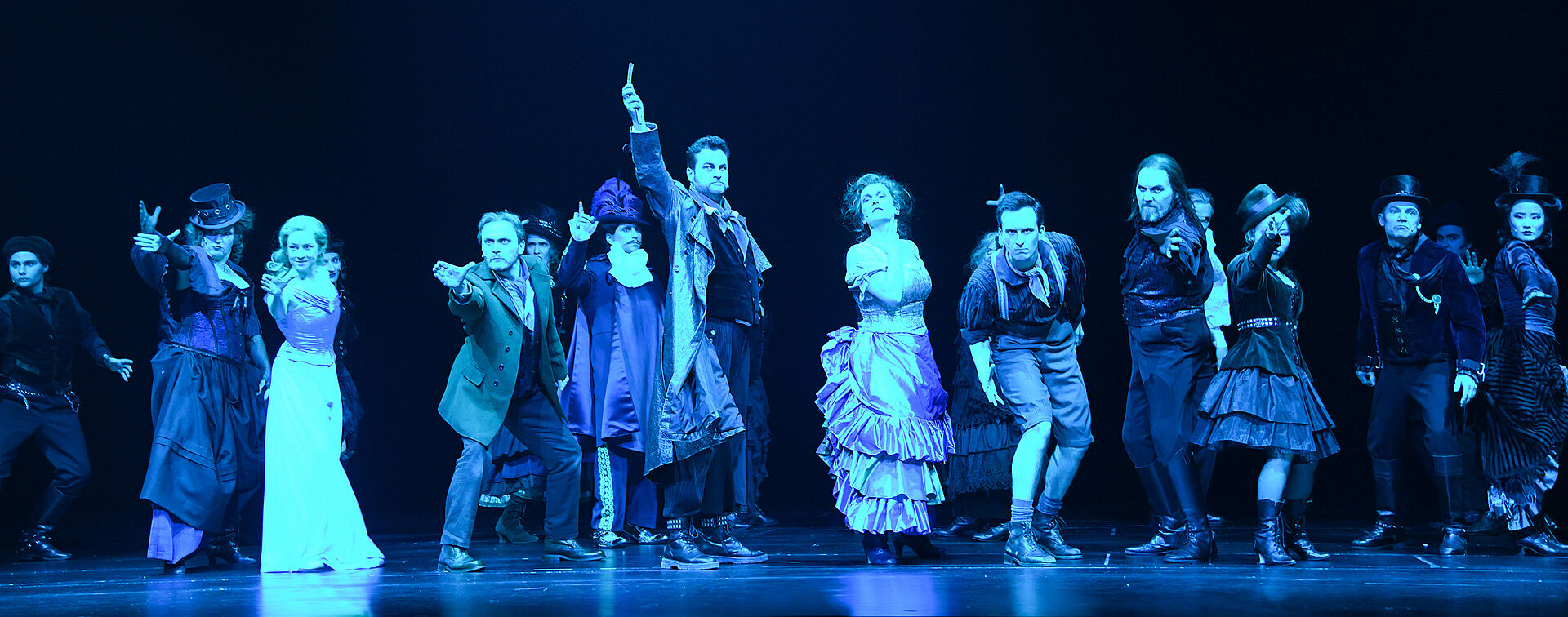 Zu sehen ist eine Gruppe von Menschen, die alle eine Hand nach vorne strecken. Der Protagonist steht im Mittelpunkt des Bildes und hält eine Rasierklinge in der Hand.