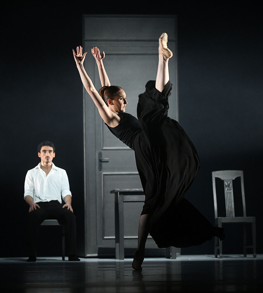 Im Hintergrund sitzt ein Tänzer. Vor ihm steht eine Frau.