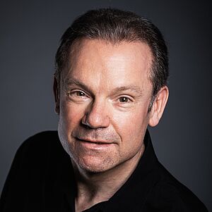 Portraitfoto von James Bobby. Er schaut von unten nach oben direkt in die Kamera. Er trägt sein Haar kurzgeschoren und ein schwarzes Hemd. Der Hintergrund ist grau.