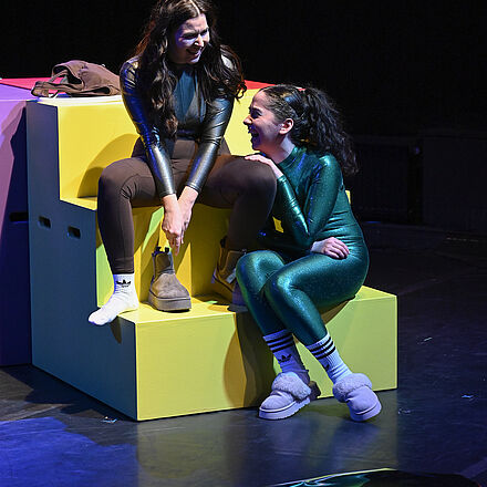 Auf der Treppe sitzen zwei Personen und lachen. Vor ihnen liegt ein Spiegel.