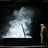 Macbeth blickt auf einen Sarg, der geöffnet ist. Daraus steigt Dampf empor.