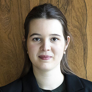 Portraitfoto von Mareike Jörling. Sie hält einen Dirigierstab vor der Brust. Ihr dunkelbraunes Haar ist halb zurückgesteckt. Sie trägt einen schwarzen Anzug, darunter ein schwarzes Oberteil.