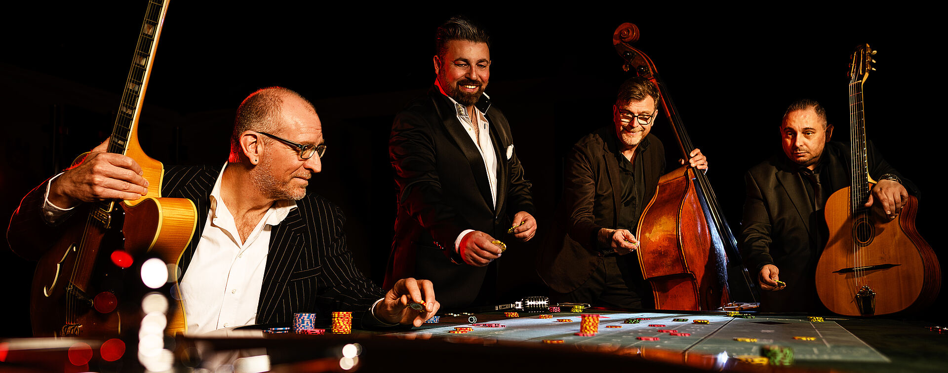 Vier Männer am Roulette-Tisch mit ihren Intrumenten. Dazu zählen Gitarren und ein Kontrabass.