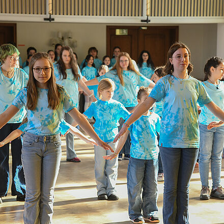 Der Kinderchor steht in mehreren Reihen mit ausgestreckten Armen. Alle tragen ein blaues Oberteil.