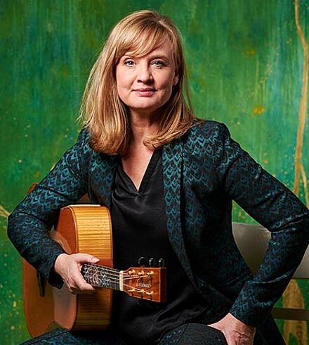 Portraitfoto von Christina Lux mit Gitarre vor grünem Hintergrund.
