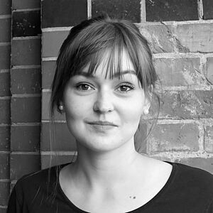 Schwarzweißes Portraitfoto von Kristýna Roháčková. Sie steht vor einer geziegelten Wand. Sie ist in ein dunkles Oberteil gekleidet. Ihr Pony fällt ihr über die Stirn. Sie trägt Perlenohrringe und lächelt dezent.