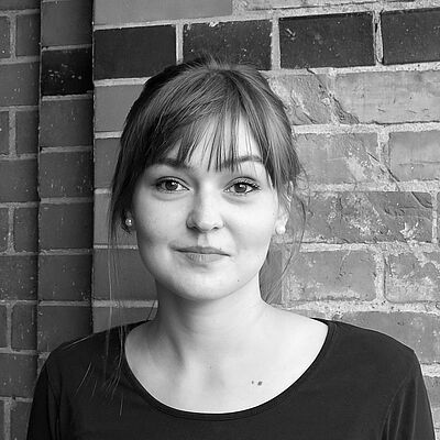 Schwarzweißes Portraitfoto von Kristýna Roháčková. Sie steht vor einer geziegelten Wand. Sie ist in ein dunkles Oberteil gekleidet. Ihr Pony fällt ihr über die Stirn. Sie trägt Perlenohrringe und lächelt dezent.