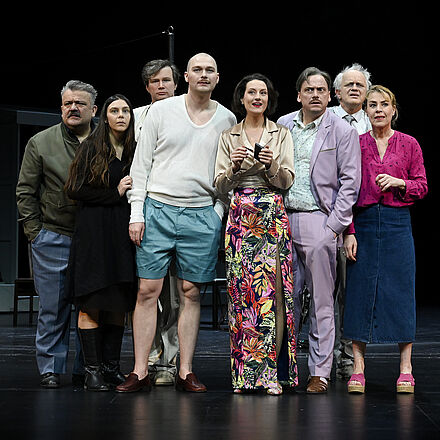 Acht Personen stehen in der Mitte der Bühne. Sie schauen fragend in die Kamera.