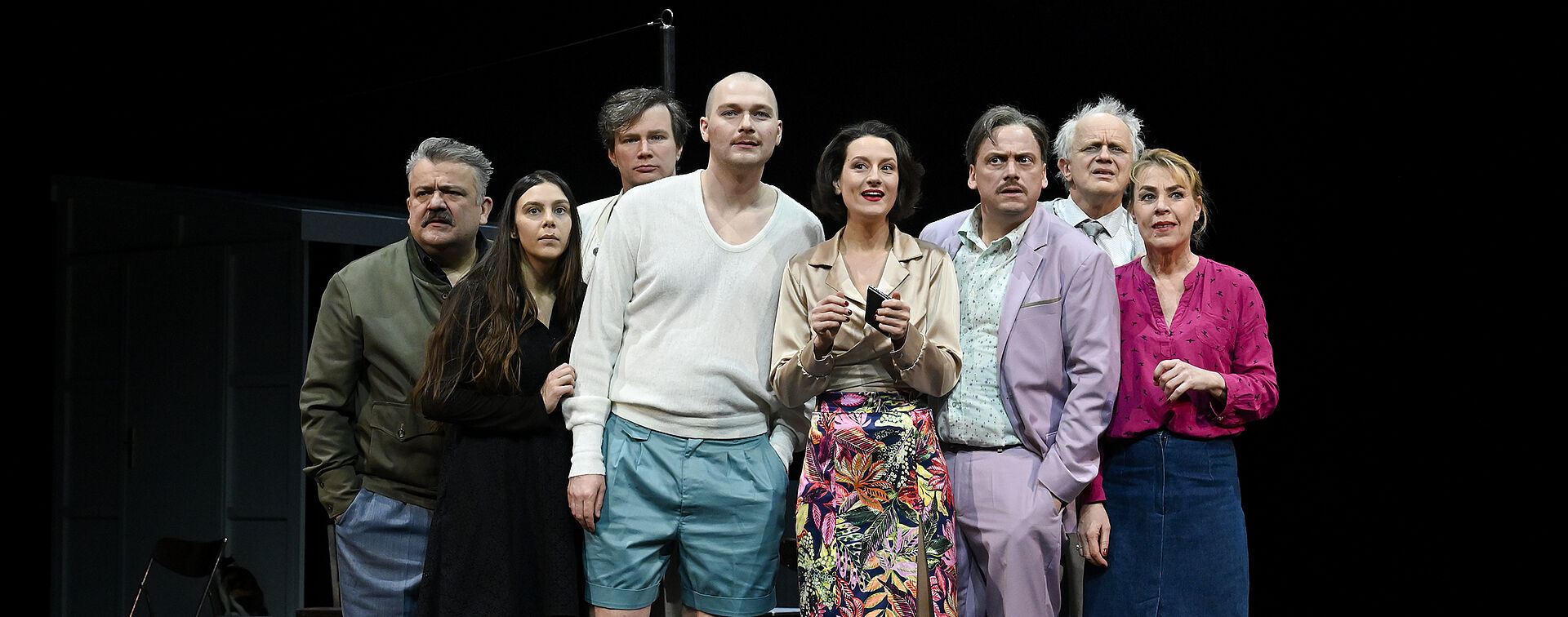 Acht Personen stehen in der Mitte der Bühne. Sie schauen fragend in die Kamera.