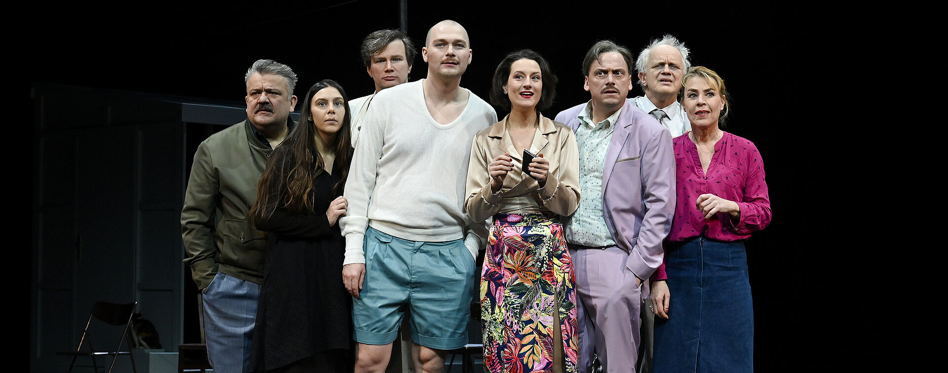 Acht Personen stehen in der Mitte der Bühne. Sie schauen fragend in die Kamera.