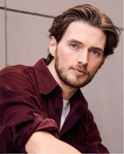 Portraitfoto von Tobias Joch. Er sitzt seitlich, der Kopf ist nach vorn gedreht. Er trägt ein rotes Hemd, darunter ein weißes T-Shirt.