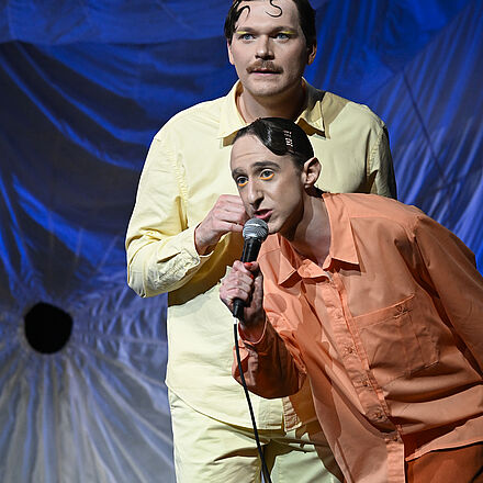 Zwei Männer halten ein Mikrofon.