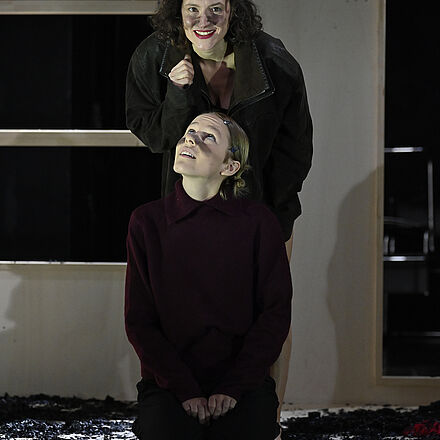 Die Frau steht hinter dem Mädchen und schaut über sie hinweg. Das Mädchen blickt zu ihr auf.