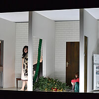 Mehrere kleine Räume sind zu sehen. Im linken steht Charlotte mit düsterem Blick. Neben ihr im mittleren Raum liegt ein Weihnachtsbaum und die am Boden hockende Sophie. Im rechten Raum liest Albert vor dem geöffneten Kühlschrank einen Brief.