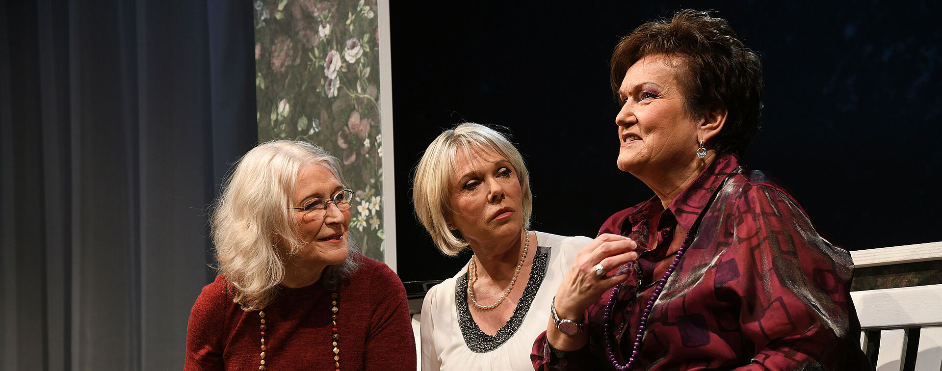 Drei Frauen sitzen auf der Bank, trinken Kaffee und sprechen miteinander.
