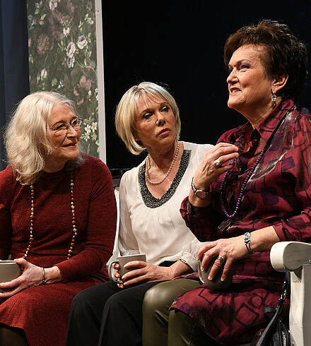 Drei Frauen sitzen auf der Bank, trinken Kaffee und sprechen miteinander.